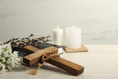 Burning church candles, rosary beads, wooden cross, Bible, willow branches and snowdrops on white table. Space for text