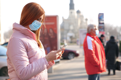 Photo of Woman with medical mask and mobile phone on city street. Virus protection
