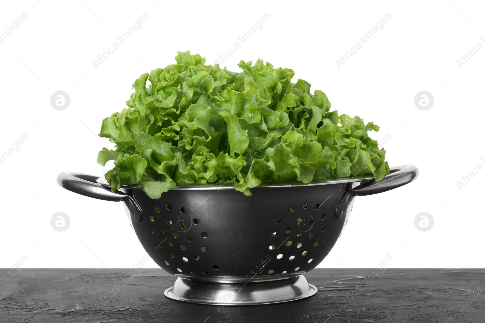 Photo of Metal colander with fresh lettuce on black textured table against white background