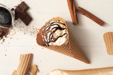 Photo of Delicious vanilla ice cream with toppings in wafer cone on white wooden table, flat lay
