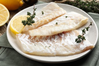 Photo of Fresh raw cod fillets with thyme and lemon on table, closeup
