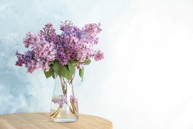 Photo of Vase with beautiful blossoming lilac on table against light background. Spring flowers