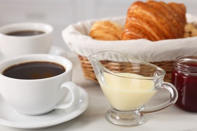 Photo of Breakfast time. Fresh croissants, coffee, sweetened condensed milk and jam on white table, closeup