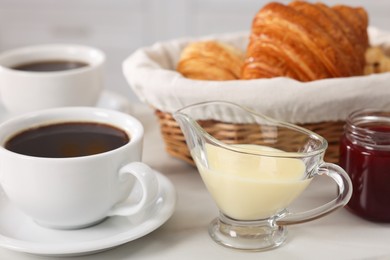 Breakfast time. Fresh croissants, coffee, sweetened condensed milk and jam on white table, closeup