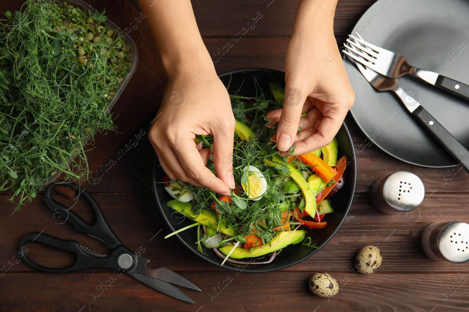 Photo of Woman making salad with fresh organic microgreen at wooden table, top view