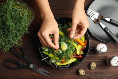 Photo of Woman making salad with fresh organic microgreen at wooden table, top view