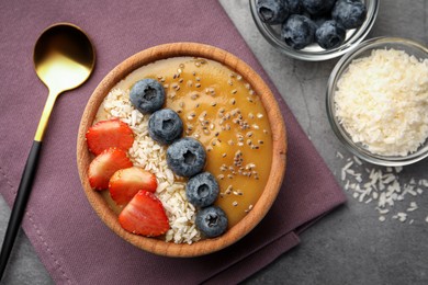 Photo of Delicious smoothie bowl with fresh berries, chia seeds and coconut flakes on grey table, flat lay