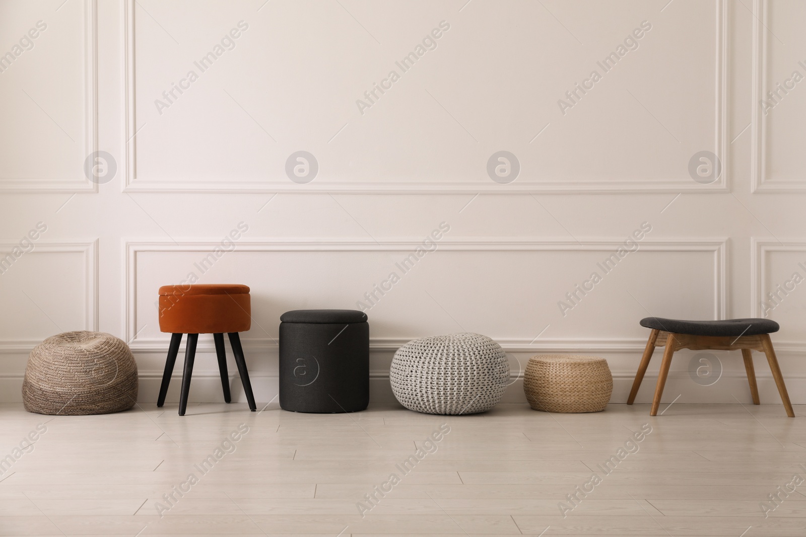 Photo of Different stylish poufs and ottomans near light wall