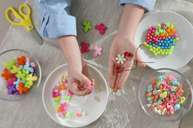 Photo of Little girl making accessory with beads at table, top view. Creative hobby