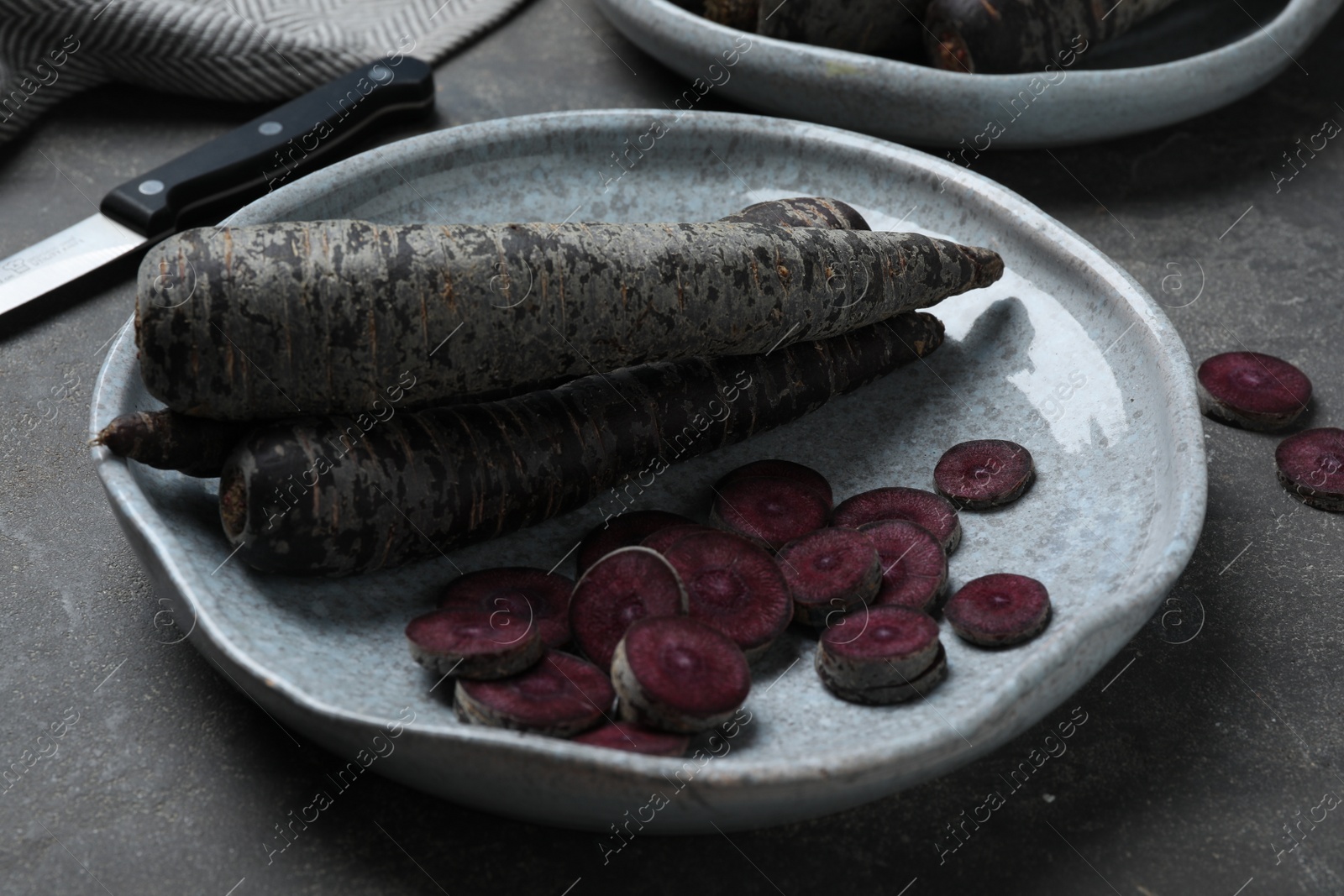 Photo of Fresh raw black carrots on grey plate