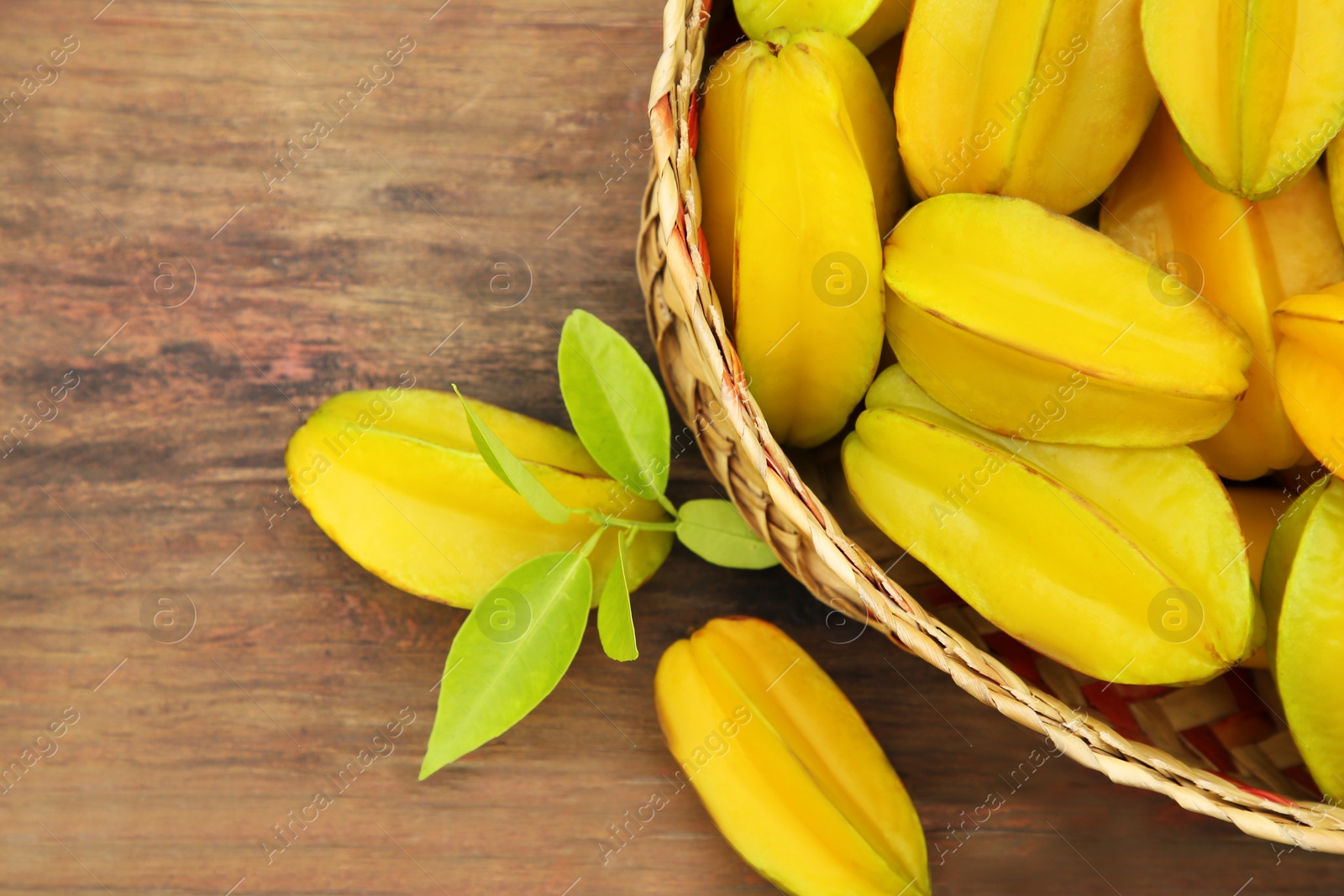 Photo of Delicious ripe carambolas in wicker basket on wooden table, top view