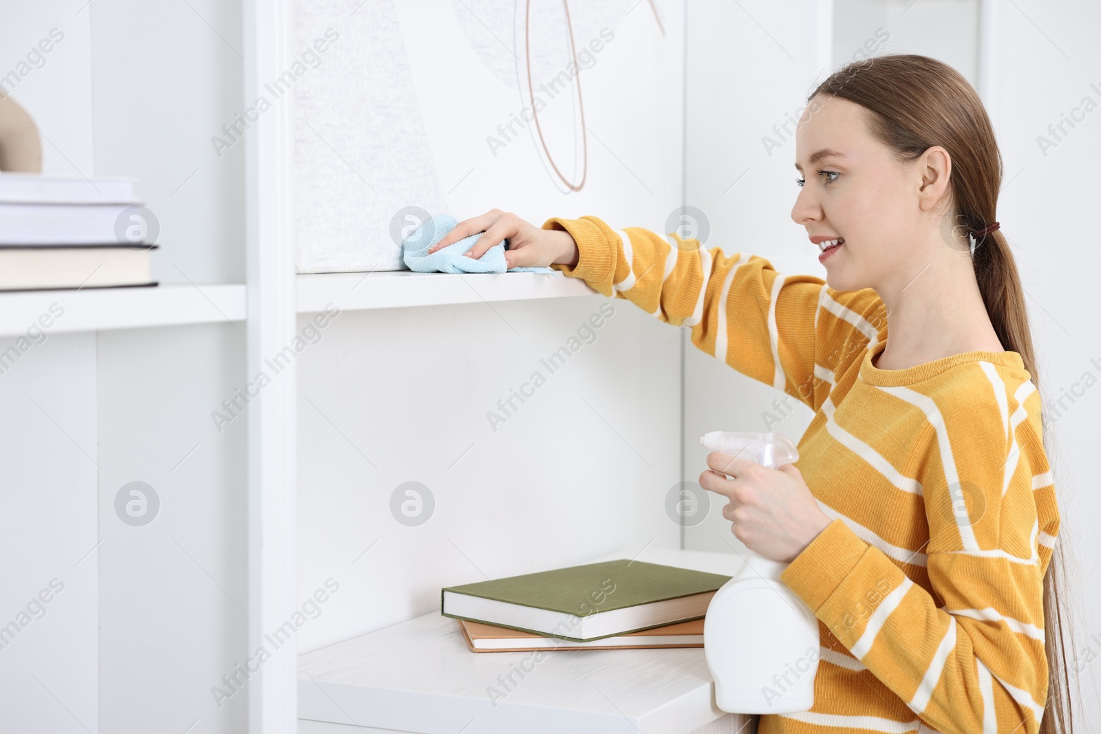 Photo of Woman with spay and rag cleaning shelf at home