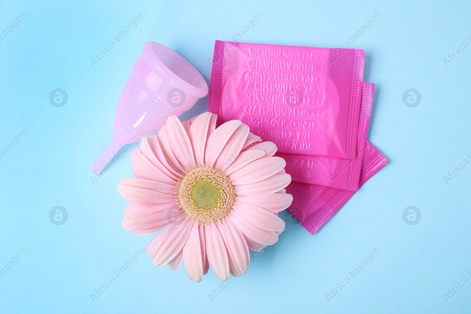 Photo of Flat lay composition with menstrual pads, cup and gerbera flower on color background. Gynecological care