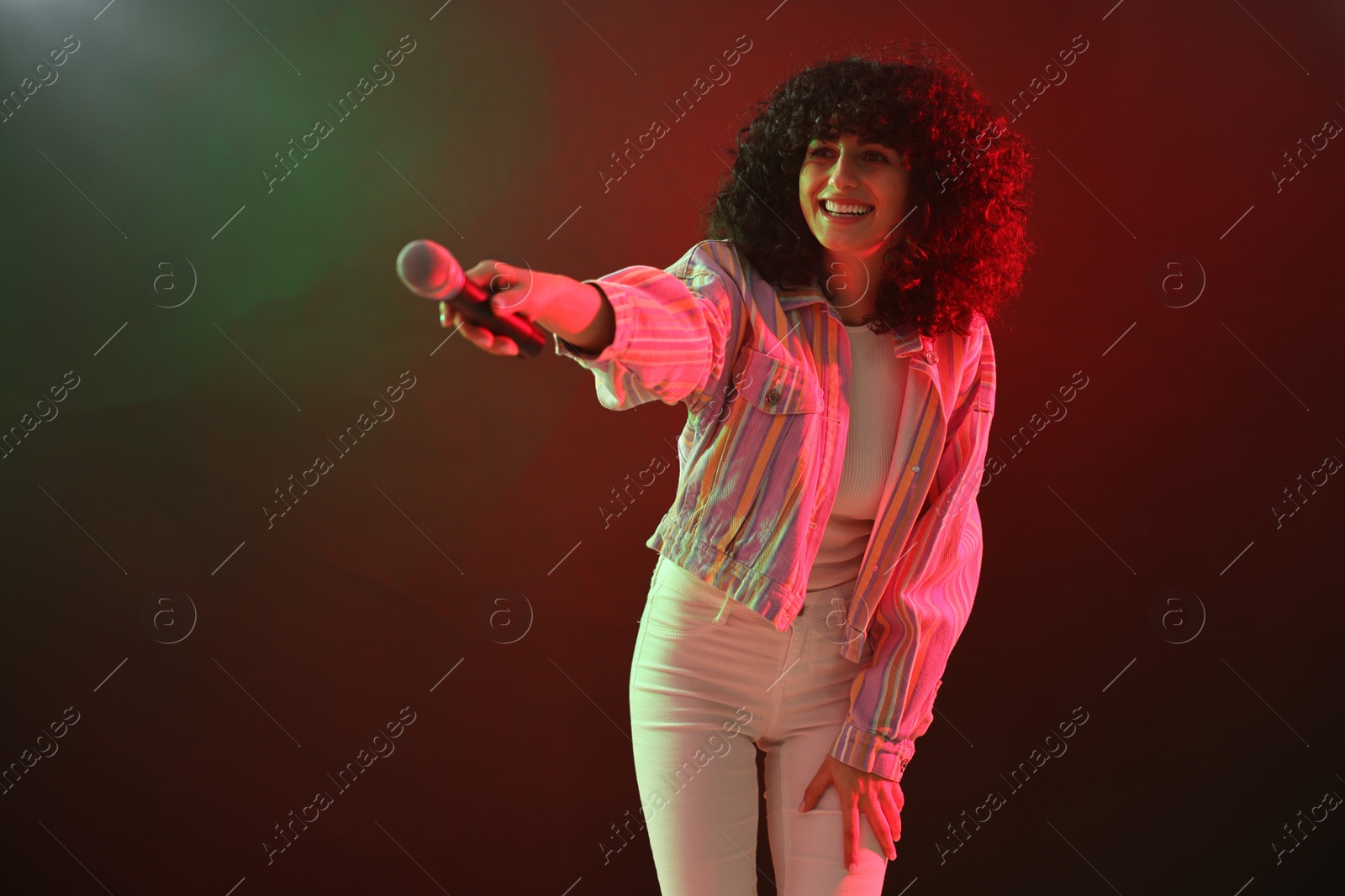 Photo of Beautiful young woman with microphone on color background in neon lights