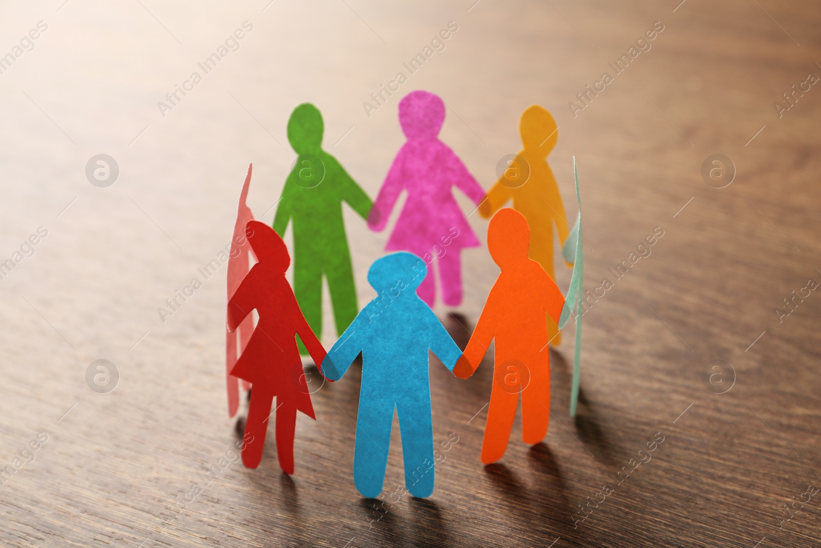 Photo of Many different paper human figures standing in circle on wooden table. Diversity and inclusion concept