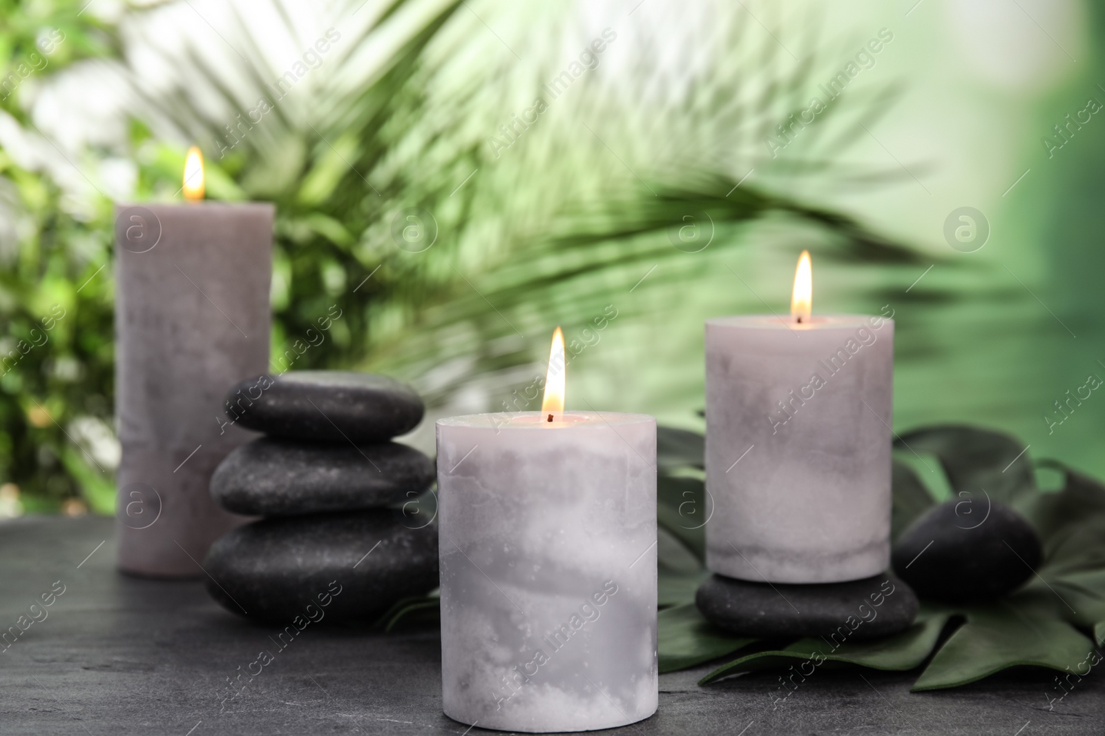 Photo of Burning candles and spa stones on grey table against blurred green background