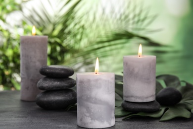 Photo of Burning candles and spa stones on grey table against blurred green background