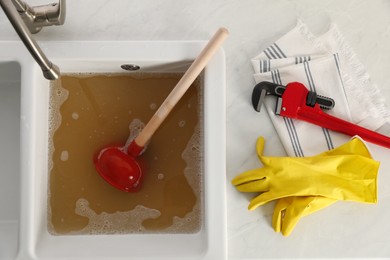 Photo of Kitchen counter with clogged sink, plunger and plumber's accessories, flat lay