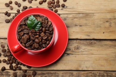 Photo of Red cup with roasted coffee beans and leaves on wooden table, flat lay. Space for text