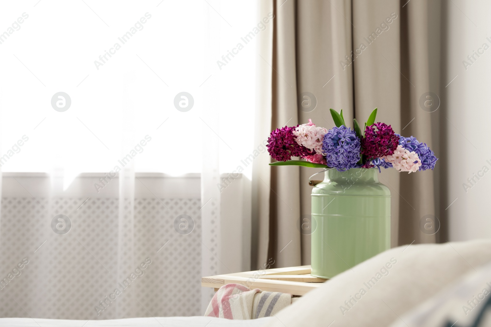 Photo of Beautiful hyacinths in metal can on wooden crate indoors, space for text. Spring flowers