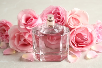 Photo of Bottle of perfume and beautiful roses on light table