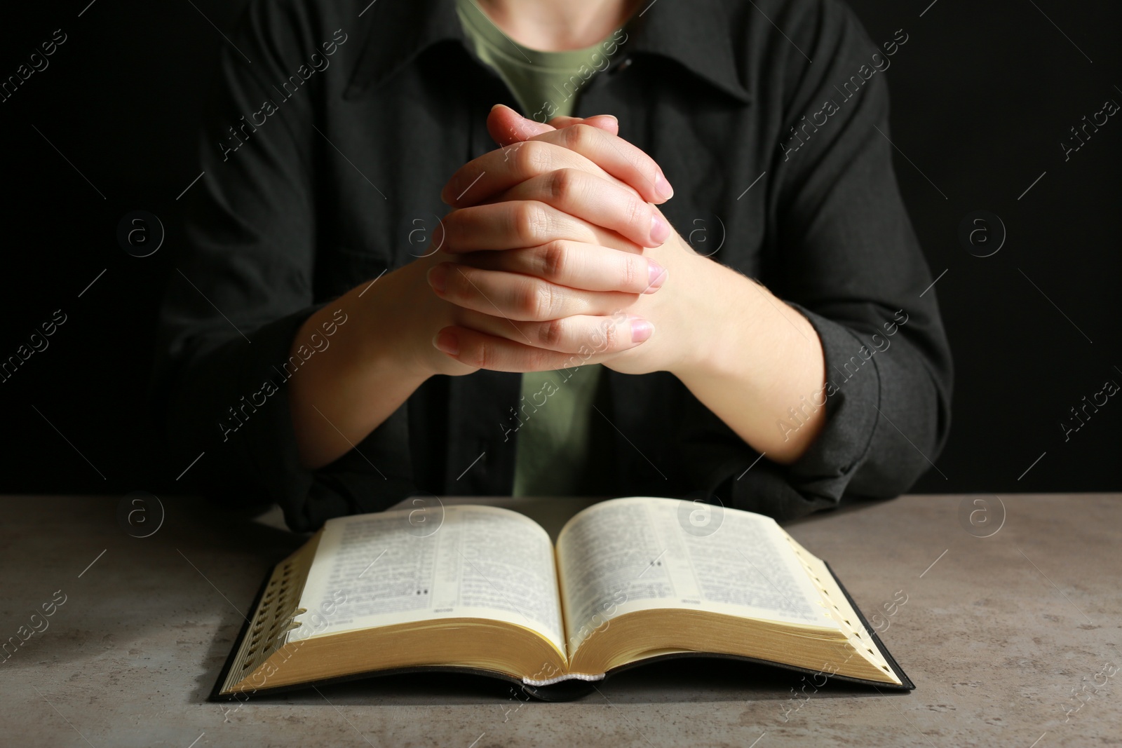 Photo of Woman praying over Bible at light grey table, closeup