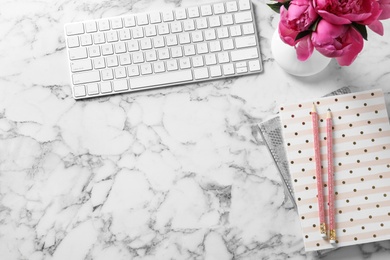 Stylish workplace with fragrant peonies on marble table, flat lay. Space for text