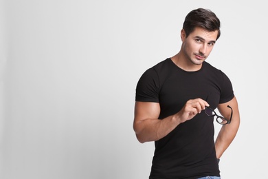 Portrait of handsome young man in black t-shirt with glasses on grey background. Space for text