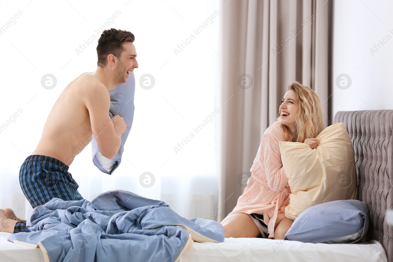 Photo of Lovely young couple having pillow fight on bed at home