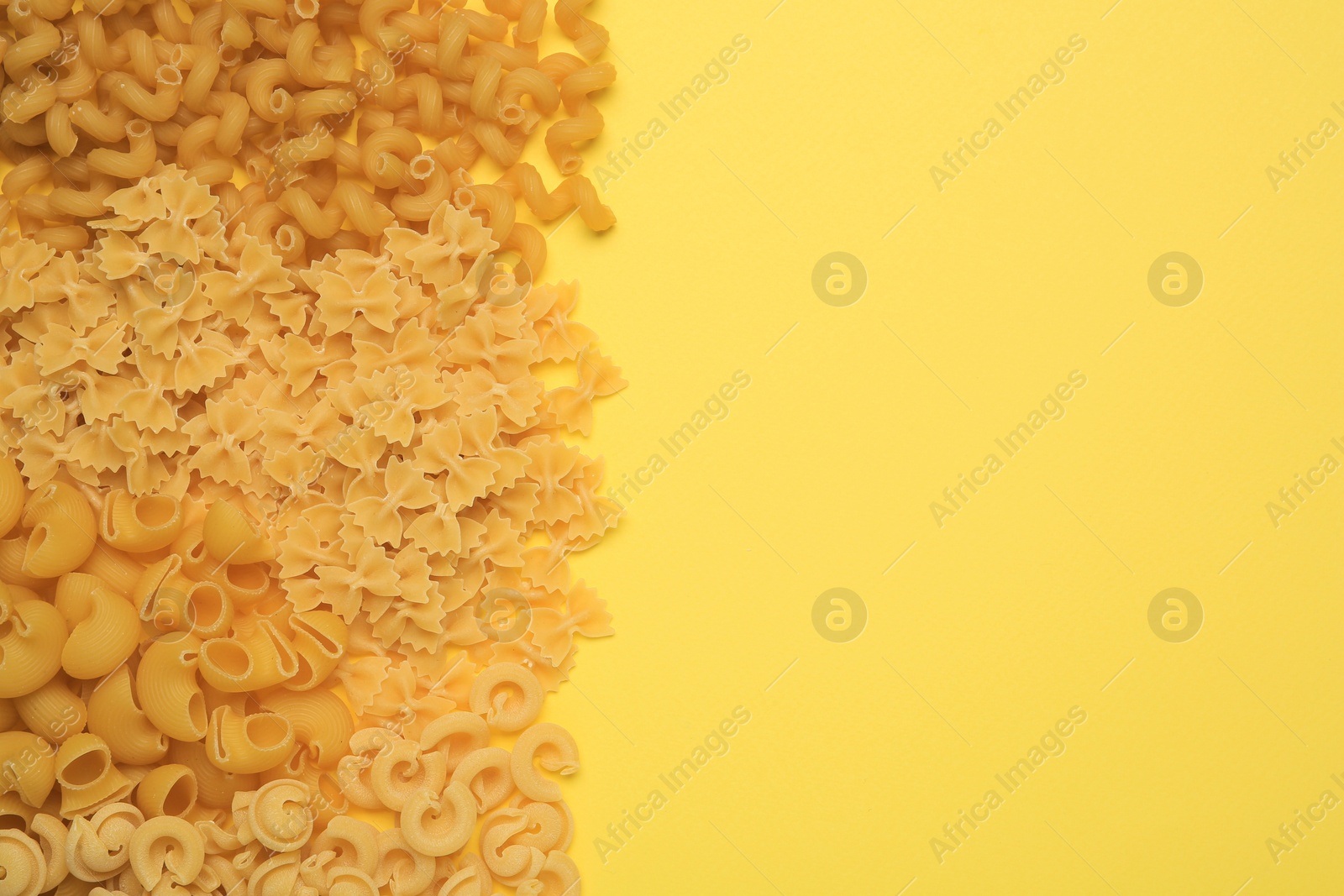 Photo of Different types of pasta on yellow background, flat lay. Space for text