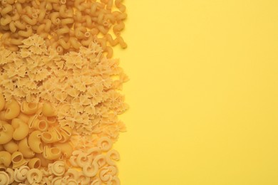 Different types of pasta on yellow background, flat lay. Space for text