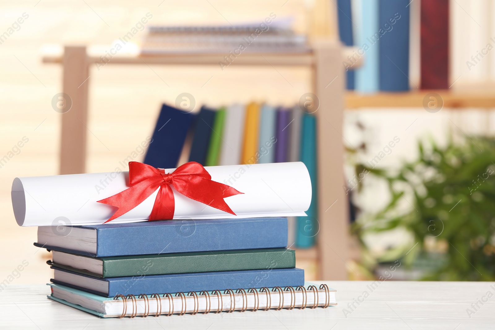 Photo of Graduate diploma with books and notebook on table against blurred background