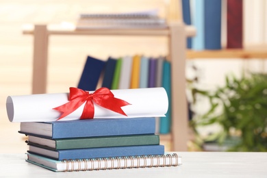 Photo of Graduate diploma with books and notebook on table against blurred background