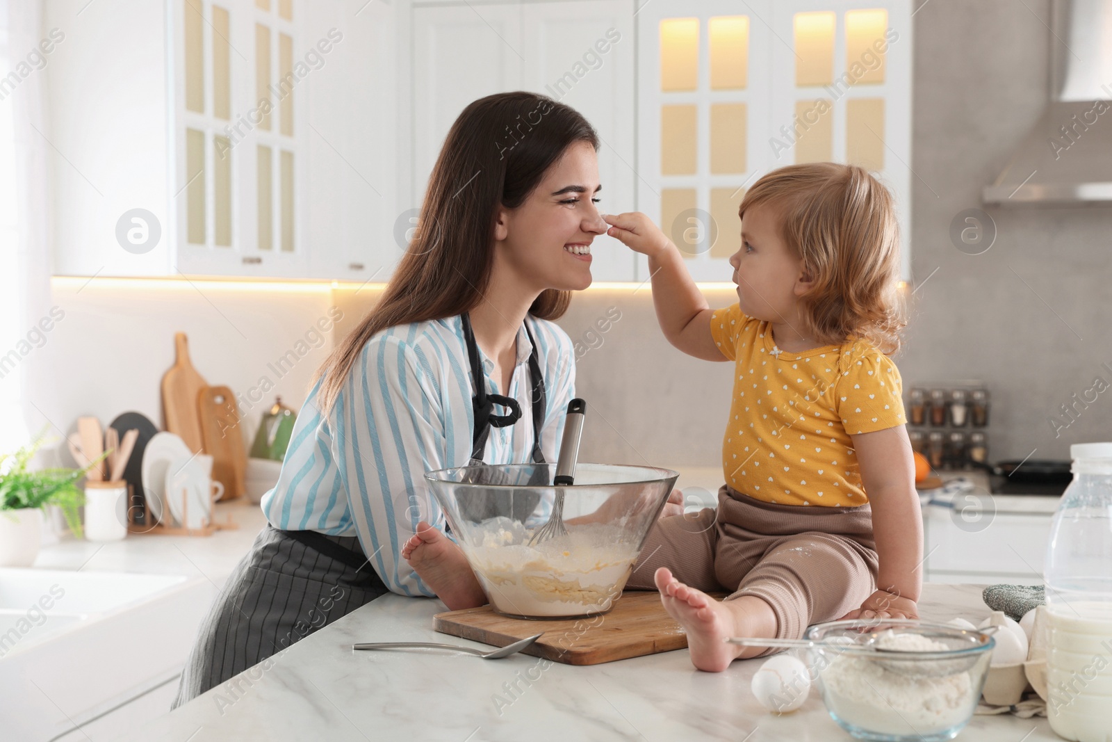 Photo of Mother and her little daughter cooking dough together in kitchen