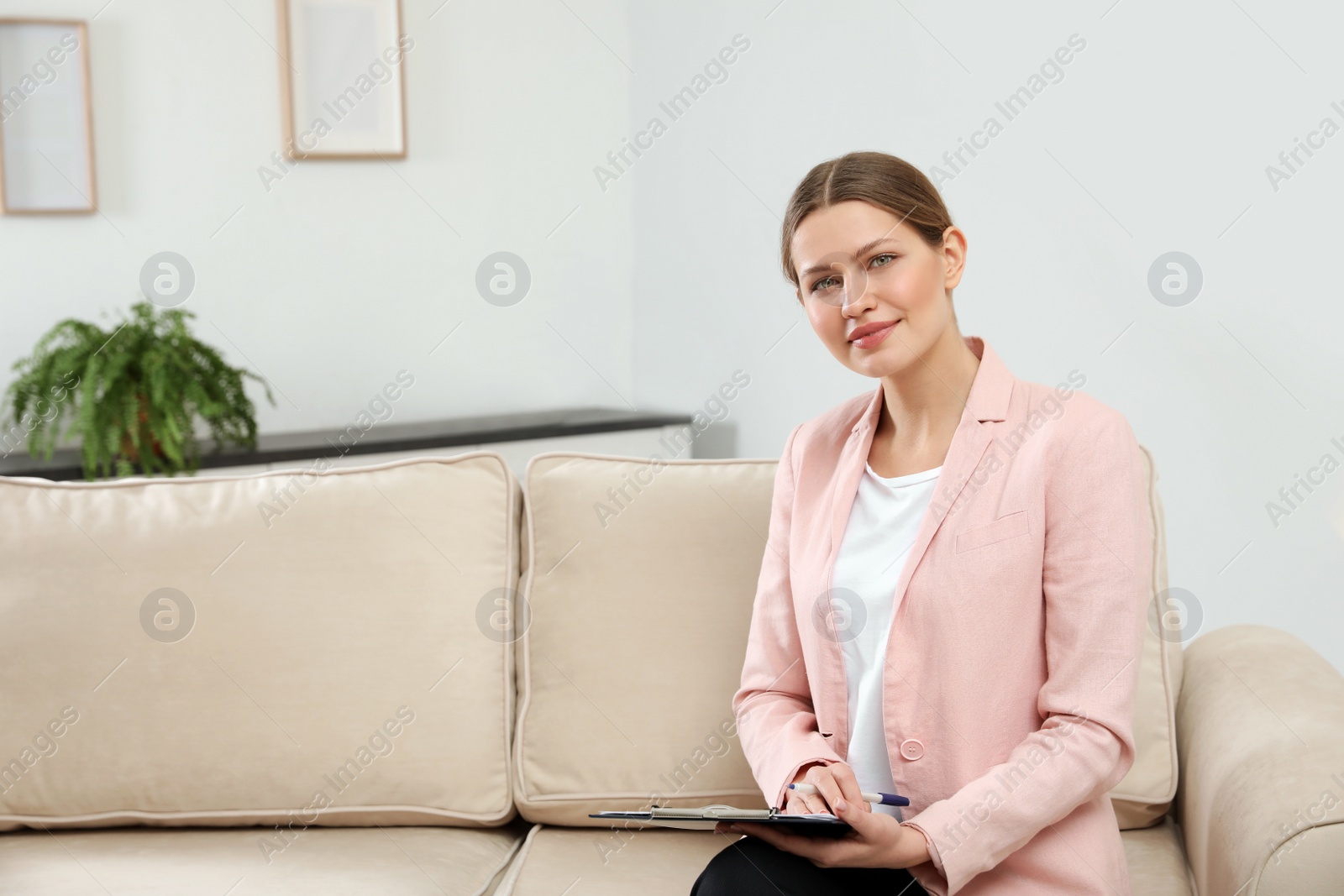 Photo of Professional psychotherapist with clipboard on sofa in office