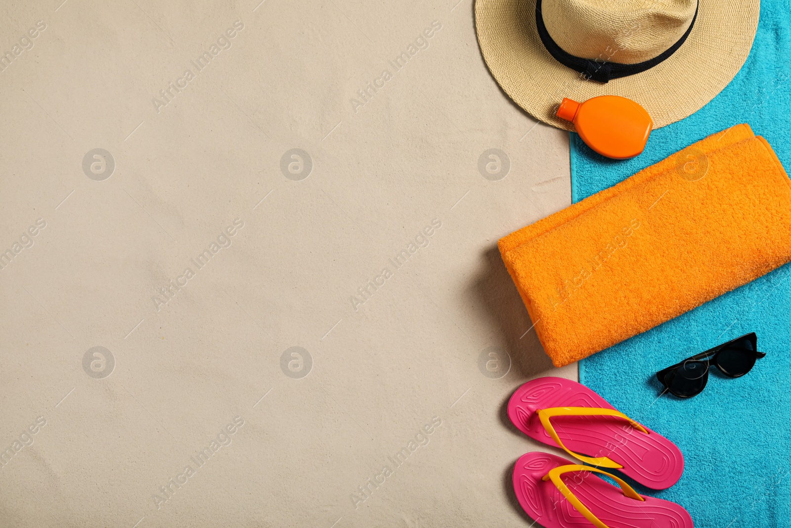 Photo of Beach towels, hat, sunscreen, sunglasses and flip flops on sand, flat lay. Space for text