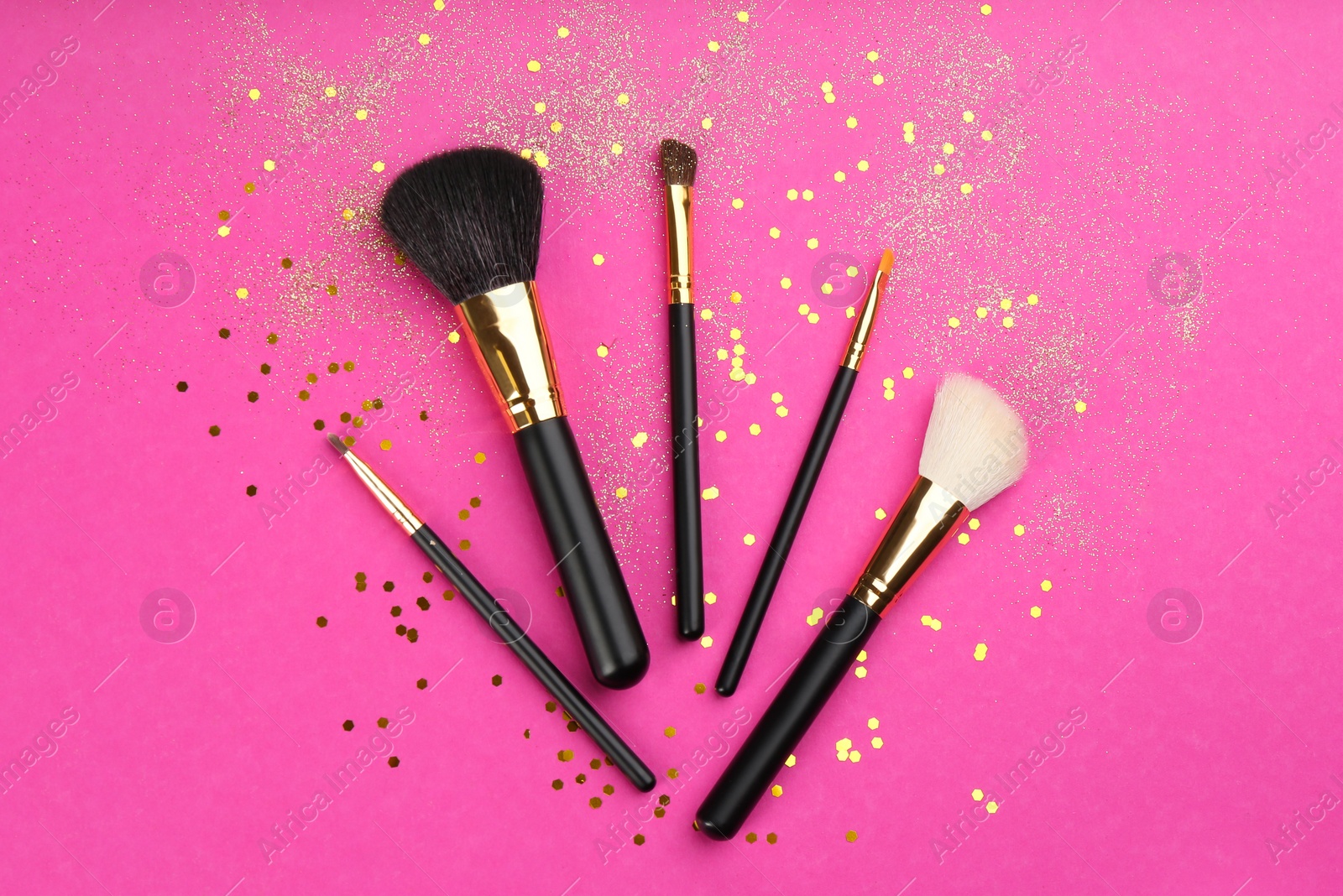 Photo of Different makeup brushes and shiny confetti on pink background, flat lay