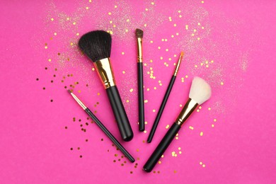 Different makeup brushes and shiny confetti on pink background, flat lay