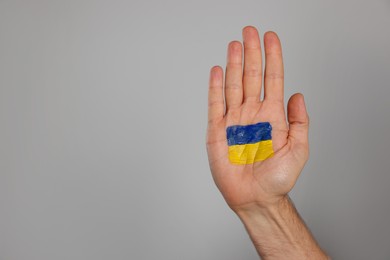 Photo of Man with drawing of Ukrainian flag on palm against light grey background, closeup. Space for text