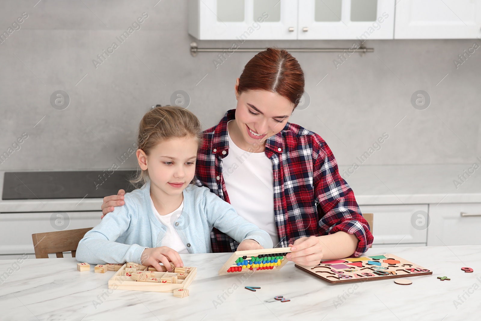 Photo of Happy mother and daughter playing with different math game kits at white marble table in kitchen. Study mathematics with pleasure