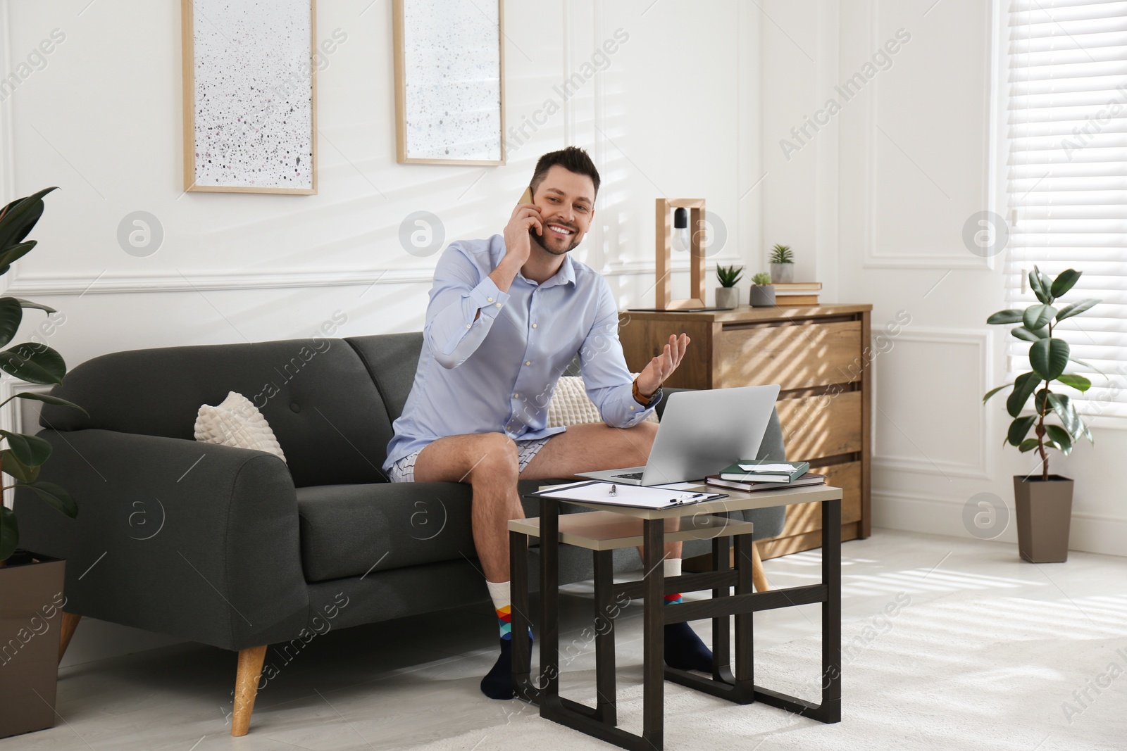 Photo of Businessman in shirt and underwear talking on phone while working with laptop at home