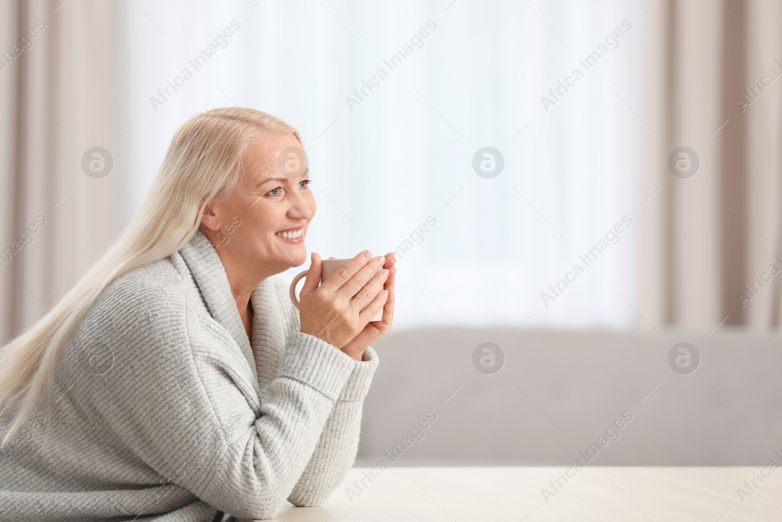 Photo of Portrait of beautiful older woman with cup of tea sitting at table indoors. Space for text