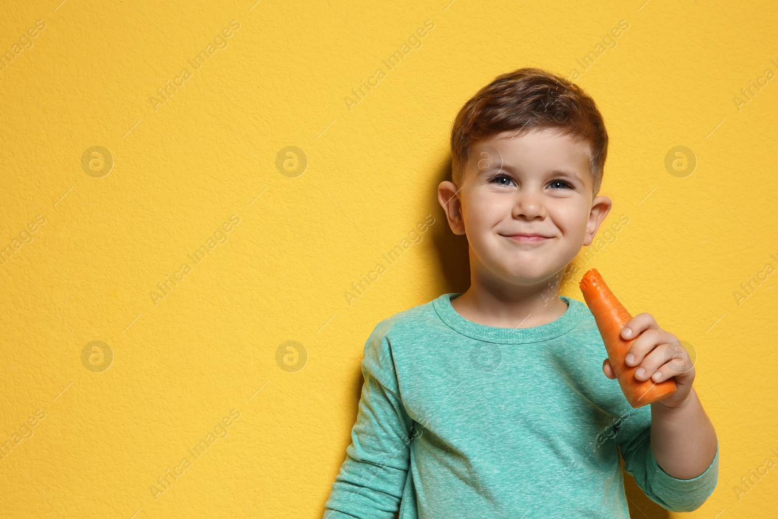 Photo of Adorable little boy with carrot on color background. Space for text