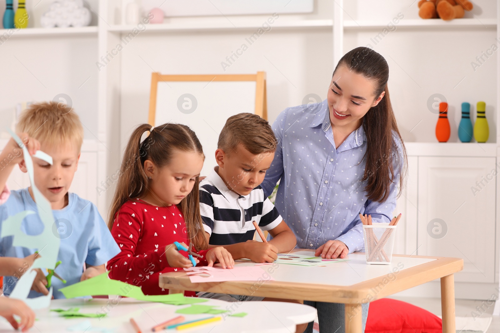 Photo of Nursery teacher and group of cute little children playing at desks in kindergarten. Playtime activities