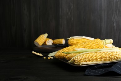 Tasty fresh corn cobs on black wooden table, space for text