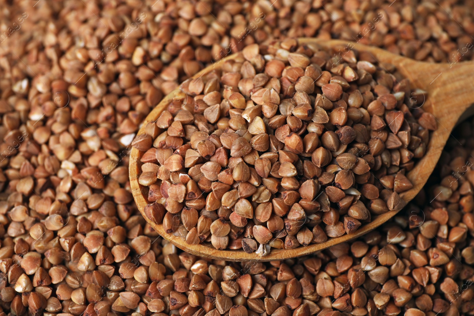 Photo of Pile of uncooked buckwheat with spoon, closeup