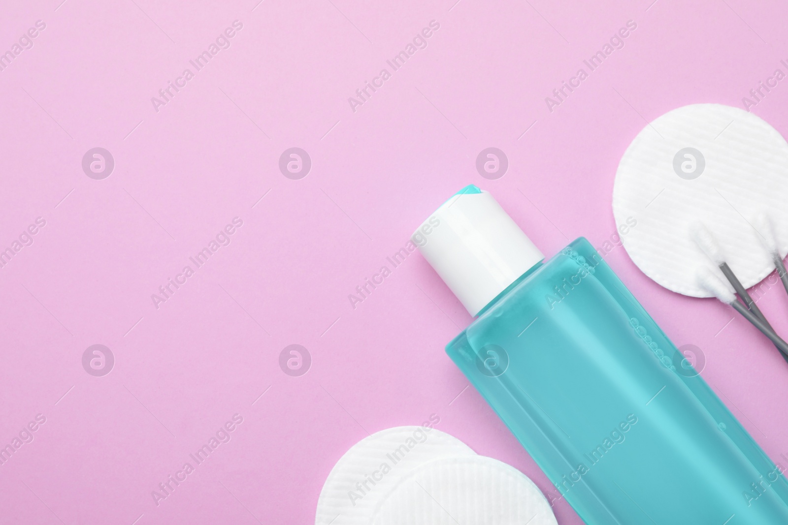 Photo of Bottle of micellar water, cotton pads and swabs on pink background, flat lay. Space for text