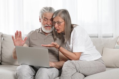Photo of Senior couple using laptop on sofa at home