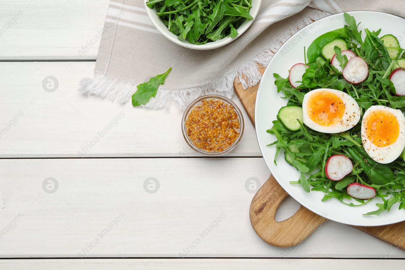 Photo of Delicious salad with boiled egg, vegetables and arugula served on white wooden table, flat lay. Space for text