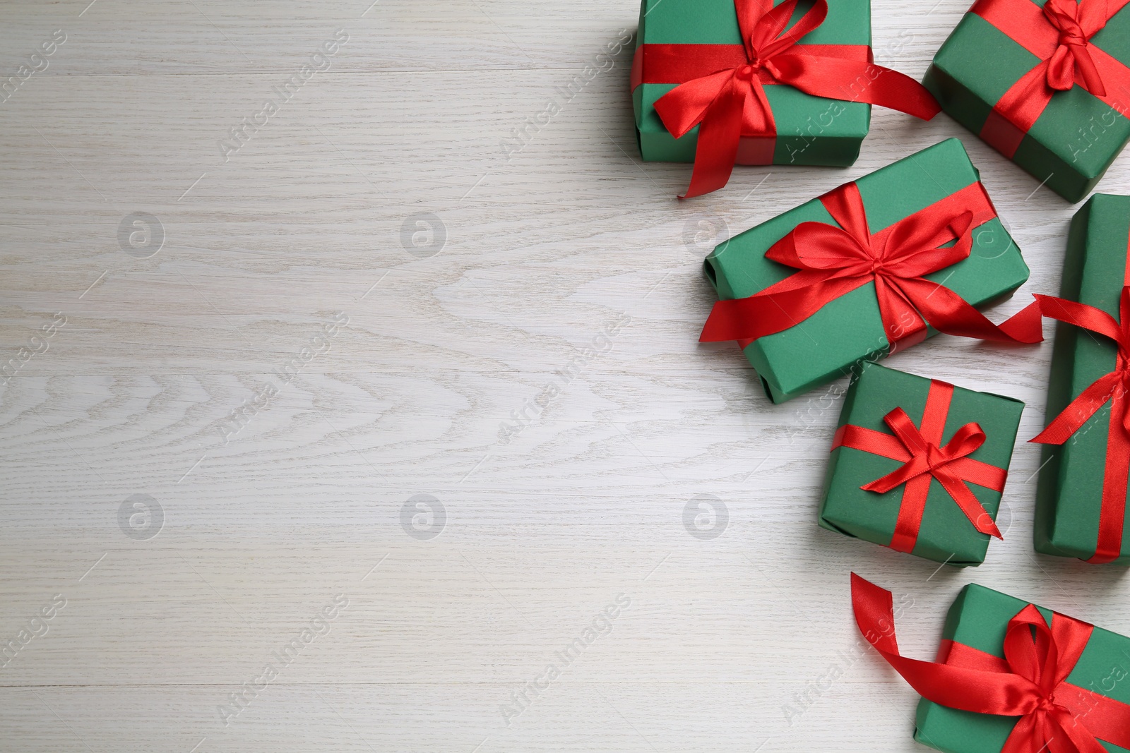 Photo of Many green gift boxes with red bows on white wooden table, flat lay. Space for text